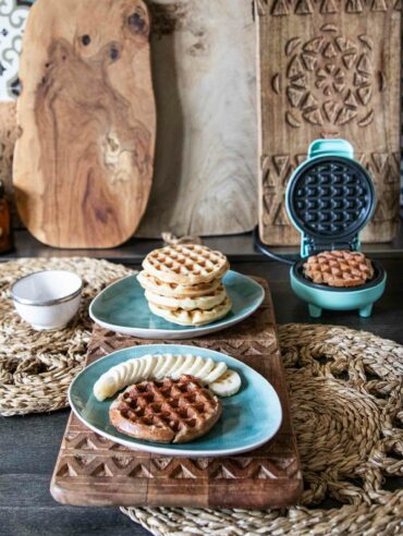 Kodiak Proteinwaffeln mit Bananenscheiben vor einem Waffeleisen auf rustikalem Tisch.