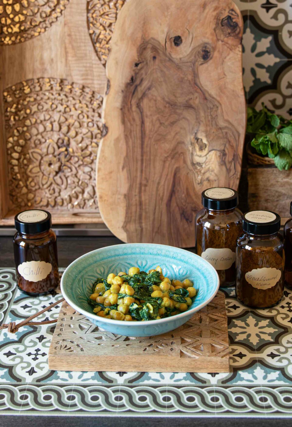 Cremiger Spinat mit Kichererbsen und Curry, umgeben von Gewürzen und rustikalen Dekoelementen