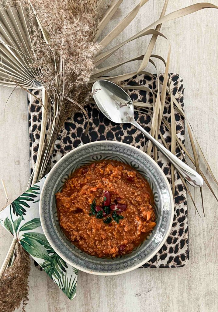 Makrofreundliches Chili mit Muskatkürbis – angerichtet in einer Schale auf Leopardenmuster, dekoriert mit Dschungelprint-Serviette und Trockenblumen. Perfekt für kalorienarme Ernährung und Makro-Tracking