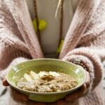 Apfel-Zimt-Porridge in einer grünen Schüssel, gehalten von einer Person mit Strickjacke.