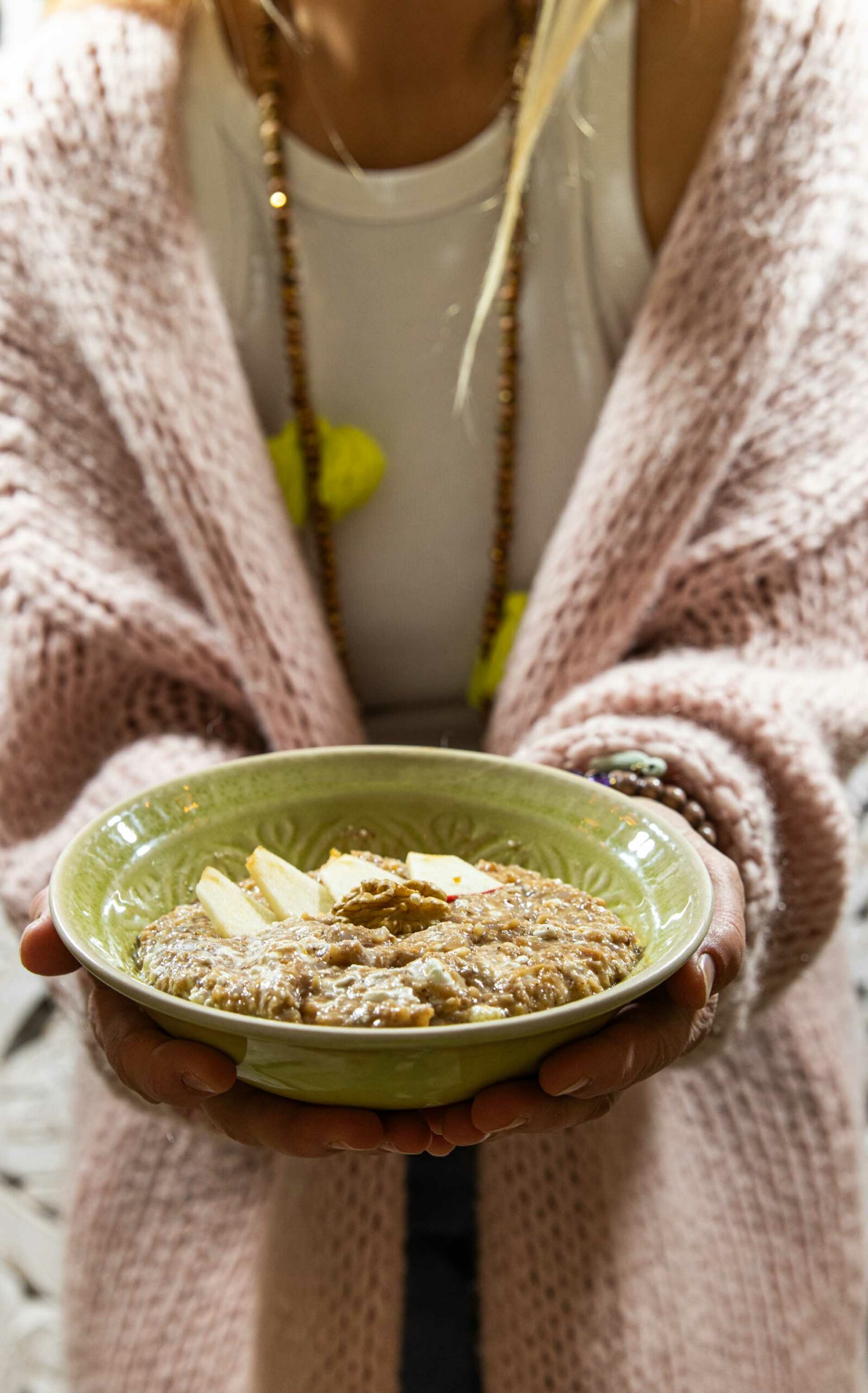 Apfel-Zimt-Porridge in einer grünen Schüssel, gehalten von einer Person mit Strickjacke.