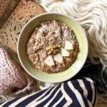 Apfel-Zimt-Porridge in einer grünen Schüssel auf flauschigem Hintergrund mit Strickjacke.