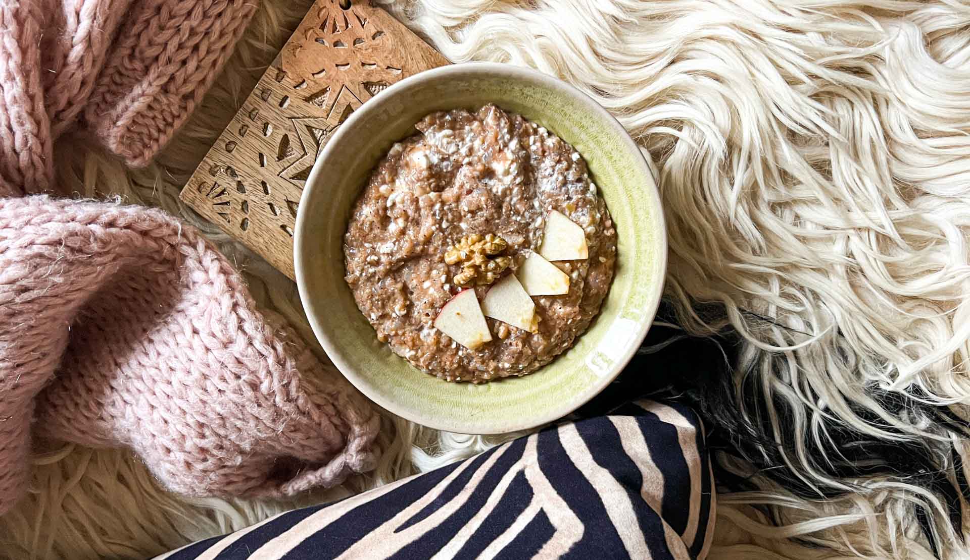 Apfel-Zimt-Porridge in einer grünen Schüssel auf flauschigem Hintergrund mit Strickjacke.