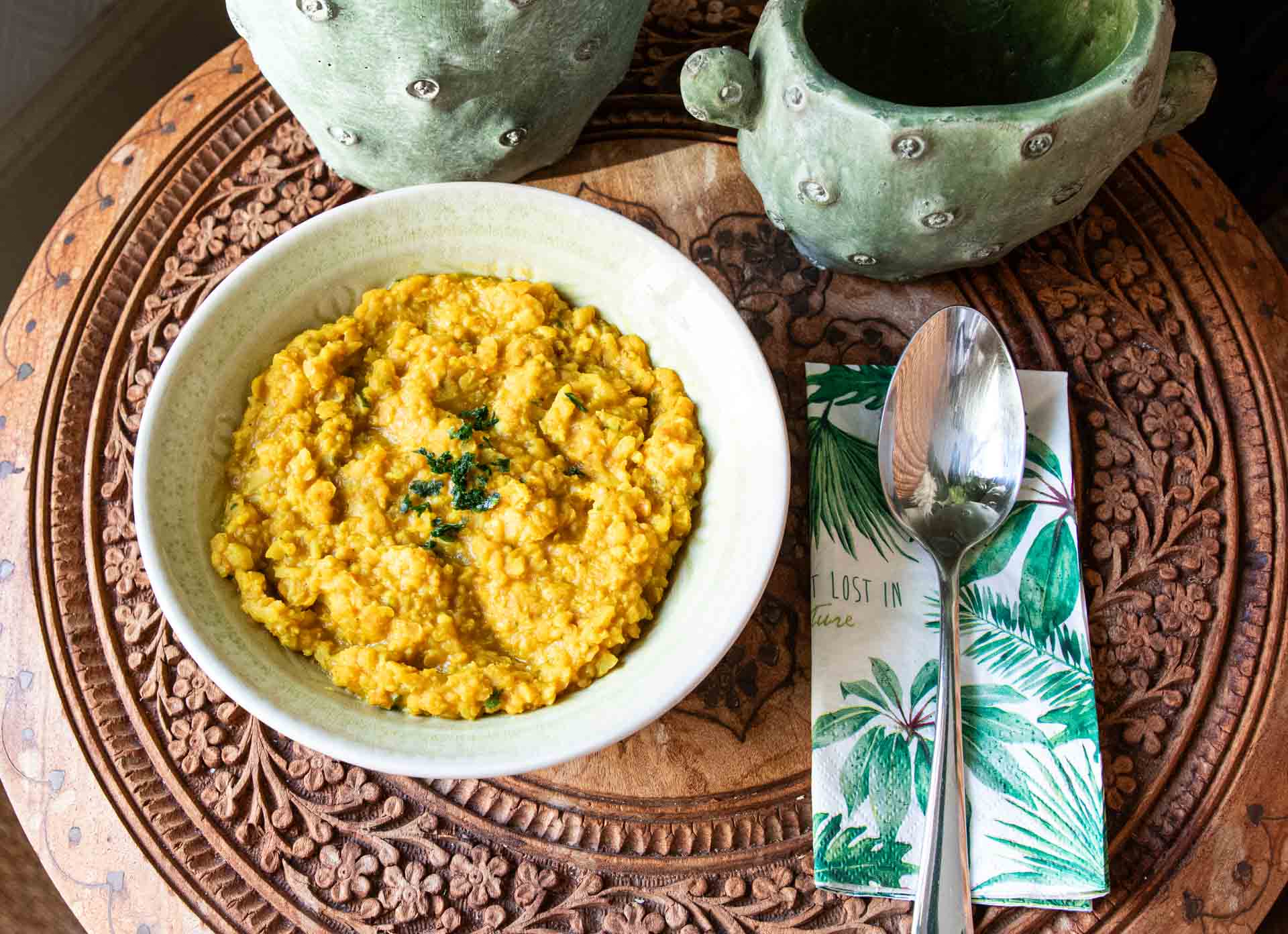 Makrofreundliches Blumenkohl-Linsen-Curry mit Kokosmilch in einer Schüssel auf einem Holztisch.