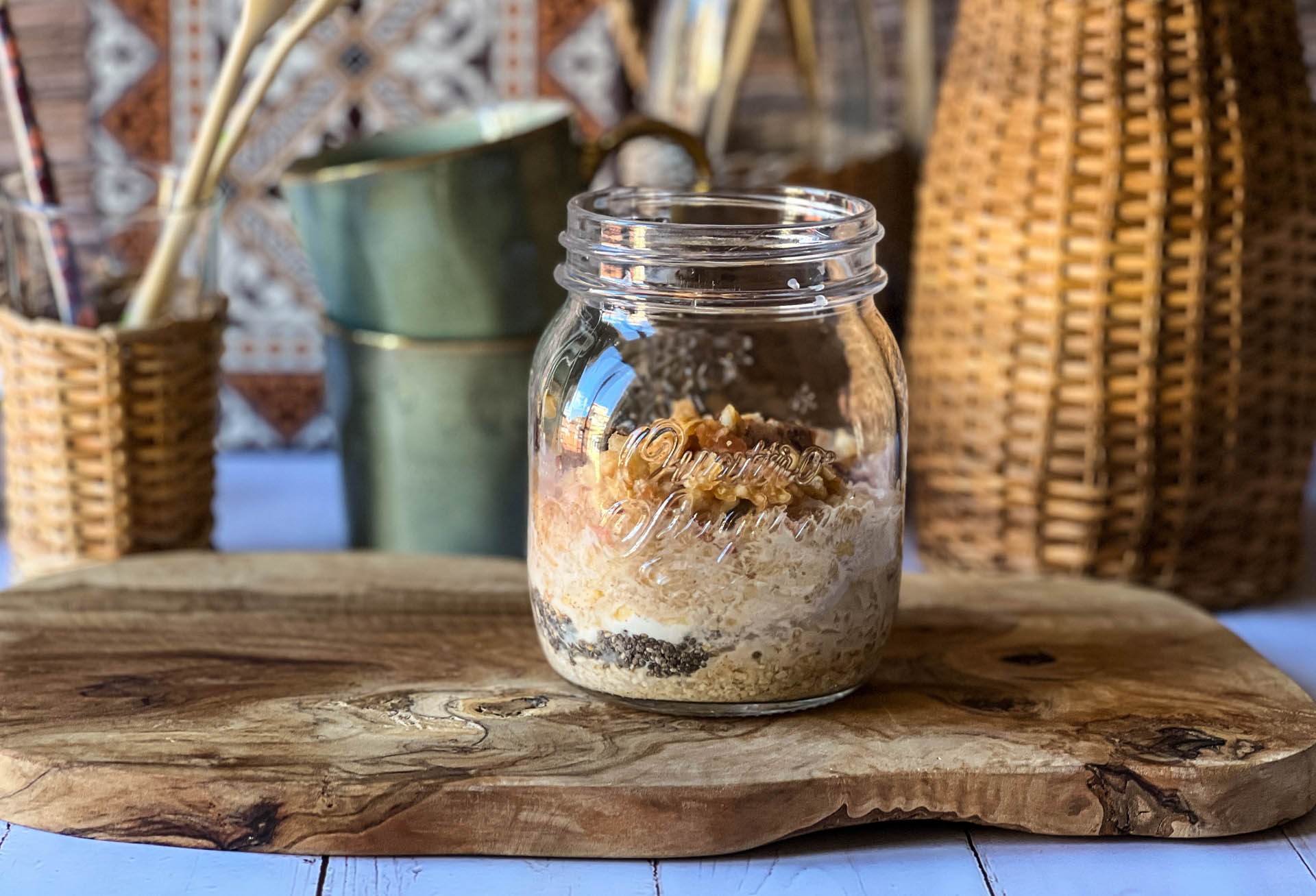 Overnight Oats mit Apfel, Zimt und Nüssen in einem Glas auf einem Holzbrett.