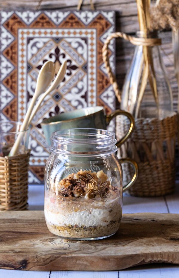 Overnight Oats im Glas mit Haferflocken, Chiasamen, Joghurt und Nüssen, angerichtet auf einem Holztisch.