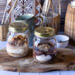 Zwei Gläser mit Overnight Oats auf einem Holztisch, umgeben von Küchendeko.