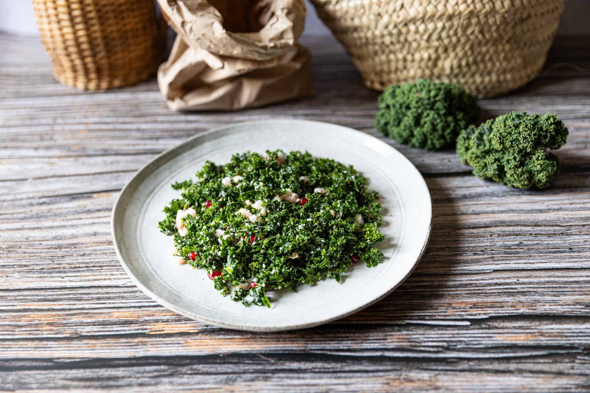 Grünkohl-Salat mit Granatapfelkernen und Parmesan, angerichtet auf einem Teller mit rustikalem Hintergrund.