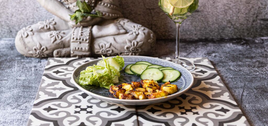 Fischchips mit Gemüse auf einem dekorativen Teller, Buddha-Statue im Hintergrund.