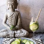 Low-Carb Airfryer Curry-Fischchips mit Gurken und Salat vor einer Buddha-Statue.