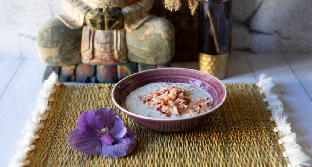 Schale mit Overnight Oats, daneben Blüte und Buddha-Statue im Hintergrund.