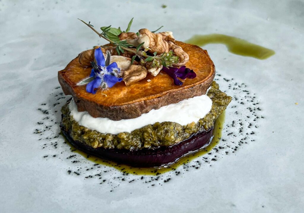 Nahaufnahme eines eleganten Süßkartoffel-Rote-Bete-Türmchens mit Kräutern und Pesto